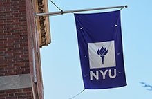 NYU Flag hanging from a building, waving in the wind